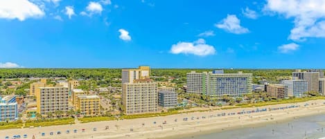 Un paysage urbain côtier avec une plage, des hôtels de grande hauteur et un ciel bleu dégagé.