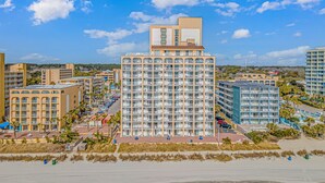 Ein mehrstöckiges Hotel mit Balkonen, einem Parkplatz und Blick auf den Strand.