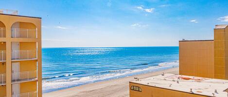 A coastal hotel with a beach view, multiple balconies, and a rooftop terrace.
