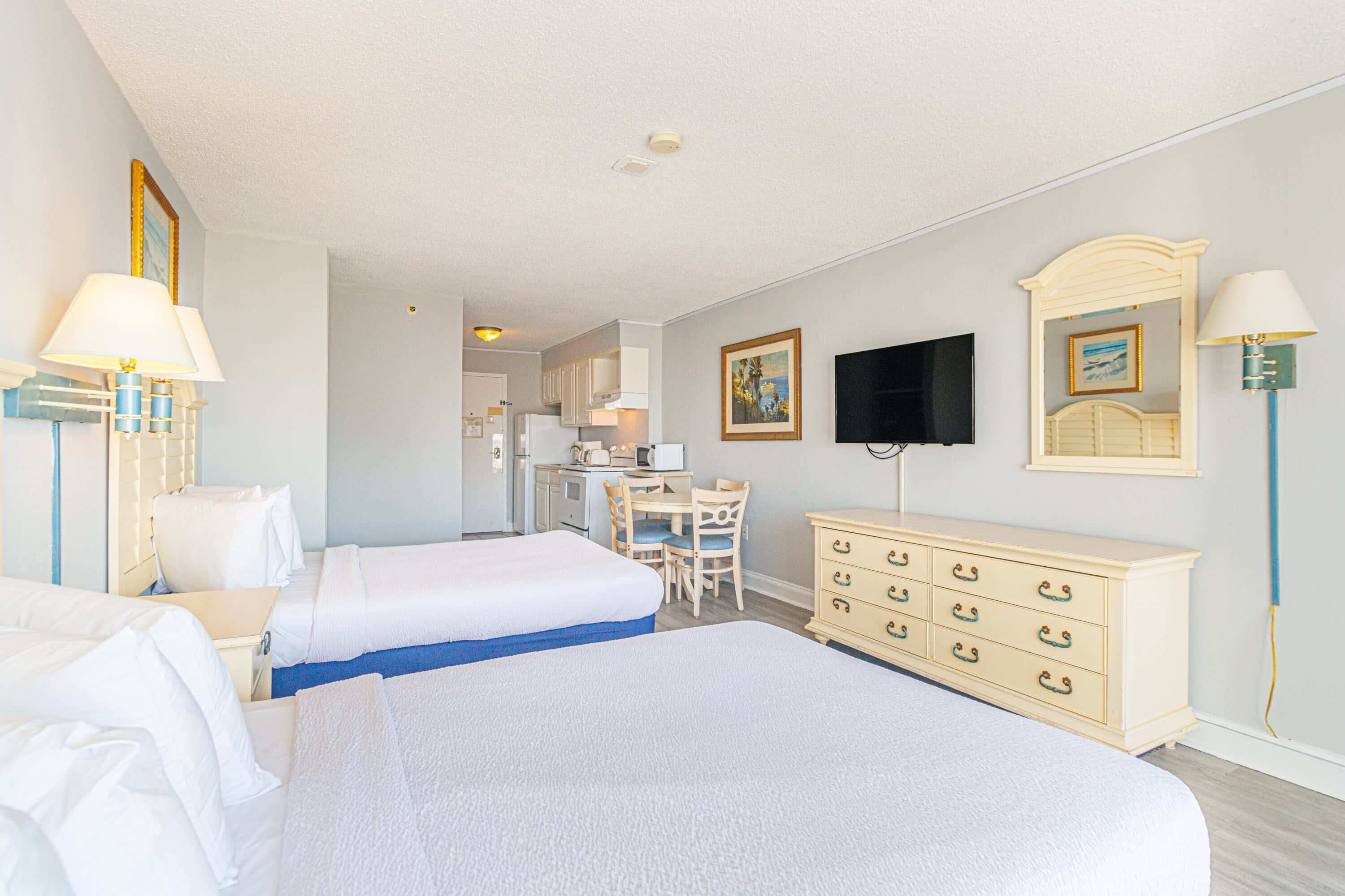 A hotel room with two beds, a desk, a dresser, a television, and a painting on the wall.