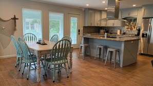 A modern kitchen with a wooden dining table, teal chairs, and a central island with stools. - 3-bedroom Riverfront home with private boat dock and view of Steinhatchee River. (Steinhatchee)