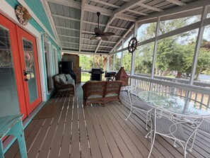 Een overdekt terras met rieten meubels, een glazen tafel en uitzicht op de omgeving.