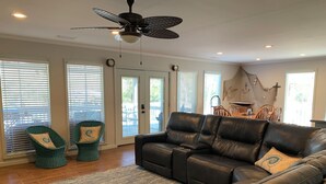A living room with a black leather sofa, two wicker chairs, a patterned rug, and a ceiling fan. - 3-bedroom Riverfront home with private boat dock and view of Steinhatchee River. (Steinhatchee)