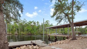 A wooden dock extending into a calm lake, surrounded by trees and pebbles. - 3-bedroom Riverfront home with private boat dock and view of Steinhatchee River. (Steinhatchee)