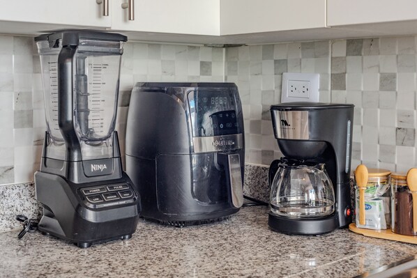 A kitchen with a Ninja blender, a coffee maker, and a glass carafe on a granite countertop.