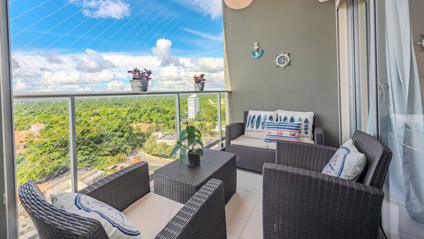 Un balcon agrémenté de meubles en osier, une vue sur la verdure et un ciel dégagé.