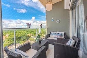 A balcony with wicker furniture, potted plants, and a view of greenery and buildings.