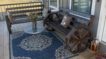 A covered porch with a wooden bench, a small table with a vase of flowers, and a decorative rug.