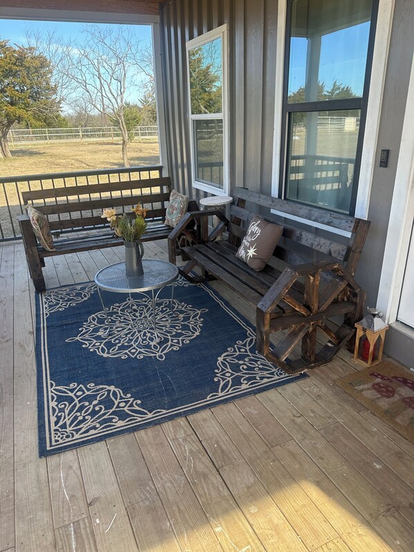 A covered porch with a wooden bench, a small table with a vase of flowers, and a decorative rug. - Charming 3-Bedroom New Home in Rice, TX – Cozy & Modern Escape! (Rice)