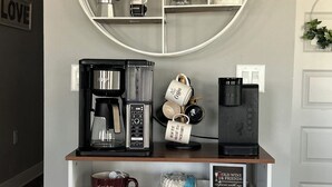 Una estación de café con un letrero decorado con motivos de café, una cafetera y varias tazas y teteras.