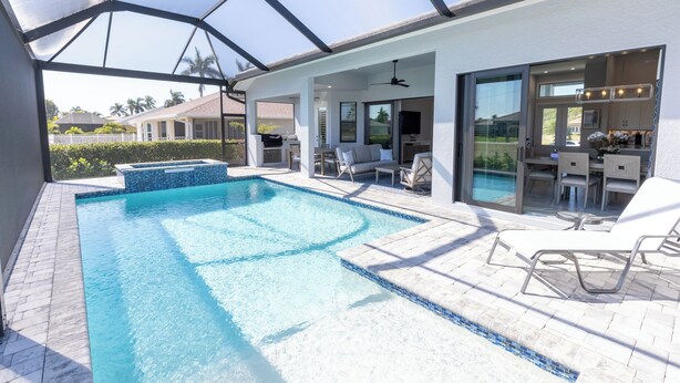 Ein Schwimmbecken mit Glasüberdachung, Gartenmöbeln und einer Terrassenfläche.