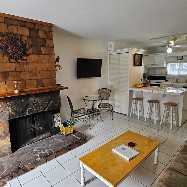 A living room with a fireplace, a TV mounted on the wall, and a kitchen area with stools and a countertop.