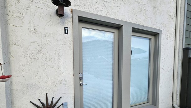 Une maison à l’extérieur beige, avec un numéro 7 sur la porte, un décor en métal représentant un soleil et un sol recouvert de neige.