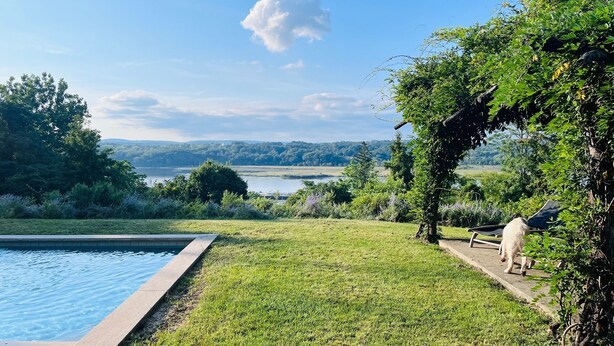 A pool with a grassy area and a view of a lake and hills. - Hudson views! (Hudson)