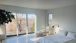A bedroom with a large bed, a chair, a desk, and a window with a view of trees and hills. - Hudson views! (Hudson)