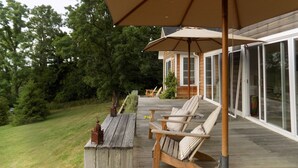 A wooden deck with outdoor furniture and a large umbrella, overlooking a house with large windows. - Hudson views! (Hudson)