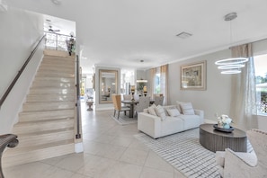 A spacious living area with a staircase, a dining area, and a modern light fixture. - Luxury  Escapes Home W/ Heated Pool & Spa  Near IMG & Siesta Key Beach (Bradenton)