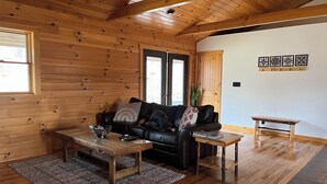 Een gezellige woonkamer met houten wanden en plafond, een zwarte leren bank, een bijzettafeltje en een klein houten bankje.