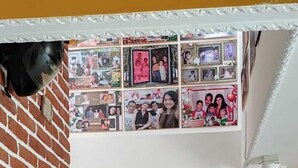 A staircase with a brick wall on one side and a white wall on the other, leading to a landing with a wall of framed photos.