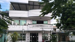 A two-story building with a balcony, a gated entrance, and a small garden area.