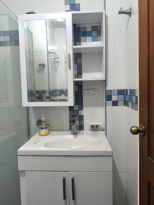 A bathroom with a white sink, a glass cabinet above it, and a door with a brass handle.