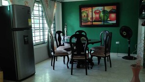 A dining area with a table and chairs, a refrigerator, and a painting on the wall.