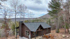 A cabin with a porch and two chairs, surrounded by trees and hills.