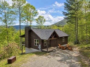 Une cabane dotée d’une véranda, d’une cheminée et offrant une vue sur la forêt et les collines environnantes.