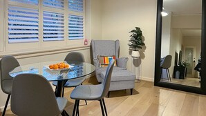 Ein Essbereich mit einem Glastisch, zwei Stühlen, einem karierten Sessel und einem Blumentopf.