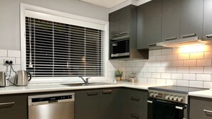 Een moderne keuken met een vaatwasser, oven en een raam met zonwering.