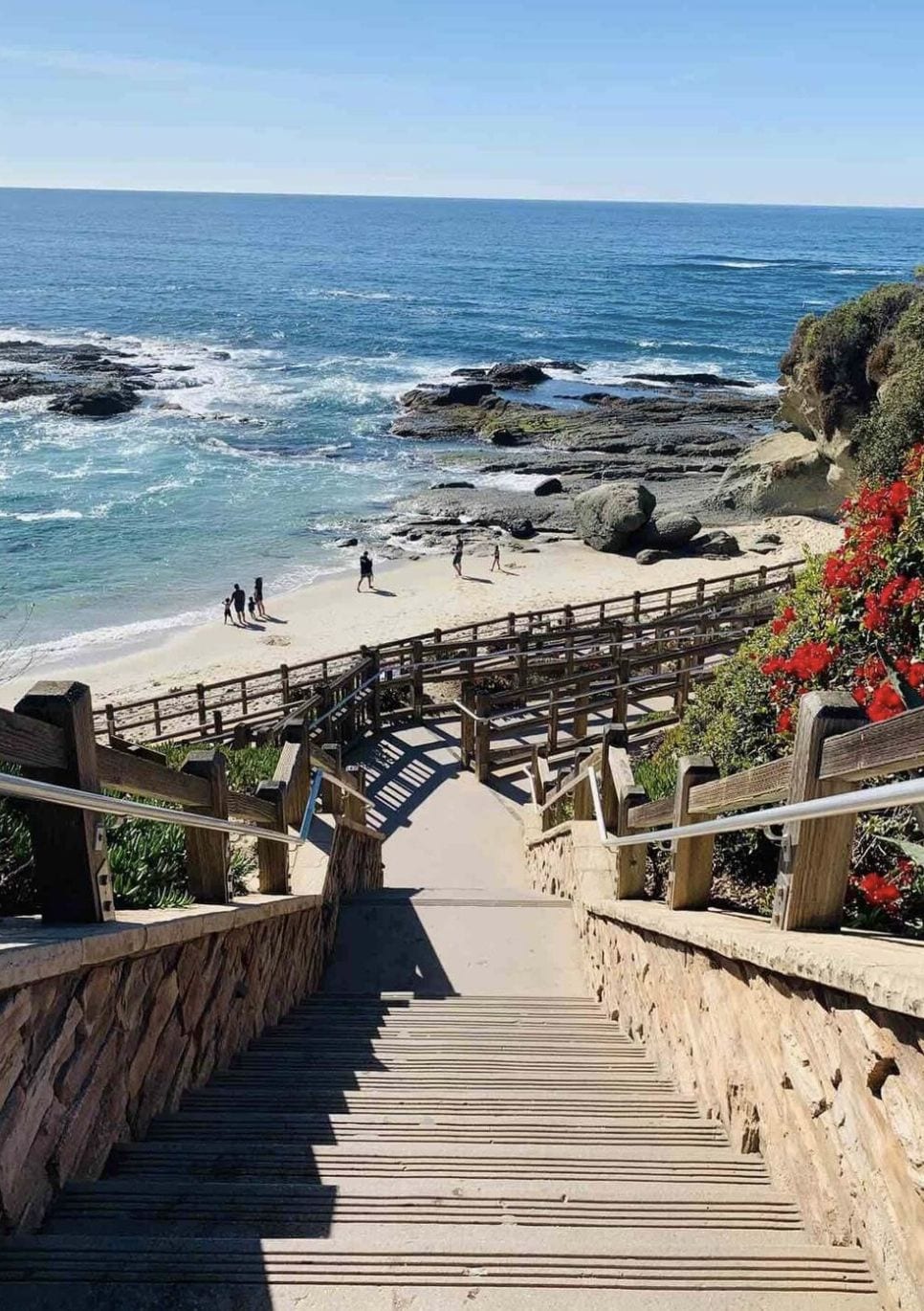 Escadaria que leva a uma praia, com corrimão de madeira e vista para o oceano.