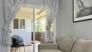 Un salon comprenant un canapé, un fauteuil et une porte-fenêtre coulissante donnant sur un espace extérieur avec une table et des chaises.