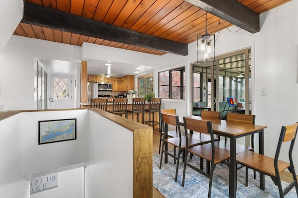 A spacious dining area with wooden tables and chairs, a kitchen in the background, and a large window with a view. - 4BR Lake Geneva, Game Room, Sleeps 16 (Lake Geneva)