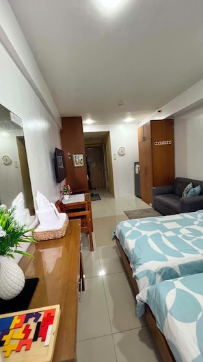 Una habitación de hotel con cama, escritorio, computadora, televisor y sofá.