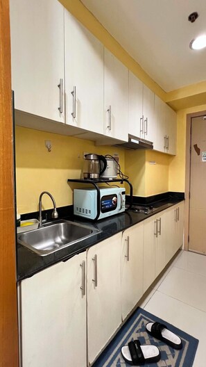 Una cocina con gabinetes blancos, encimera negra, pileta, cafetera y tostadora.