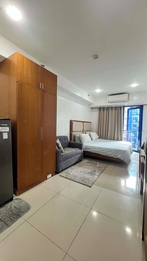 A hotel room with a bed, a sofa, a wardrobe, and a kitchenette.