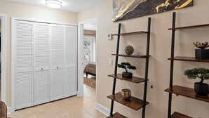 A hallway with a white closet, a wooden shelf unit with decorative items, and a painting on the wall. - Stylish & Cozy King Bed Retreat @ Baldwin Park (Orlando)