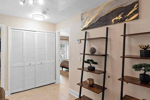 A hallway with a white closet, a wooden shelf unit with decorative items, and a painting on the wall.