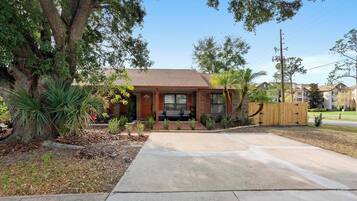 A residential house with a brick exterior, a front porch, and a driveway leading to the garage.