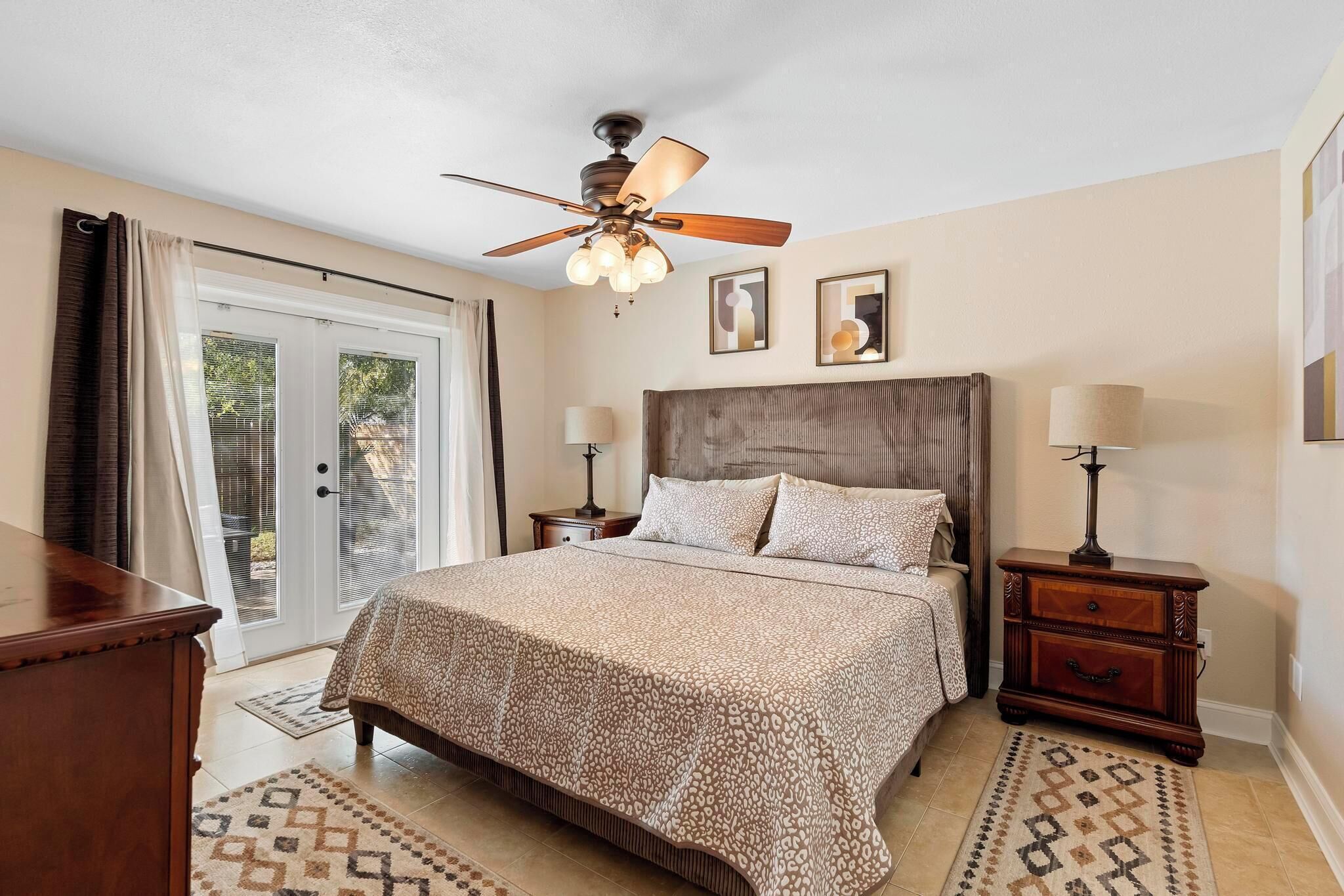 A bedroom with a bed, a ceiling fan, two bedside tables, and a window with curtains.
