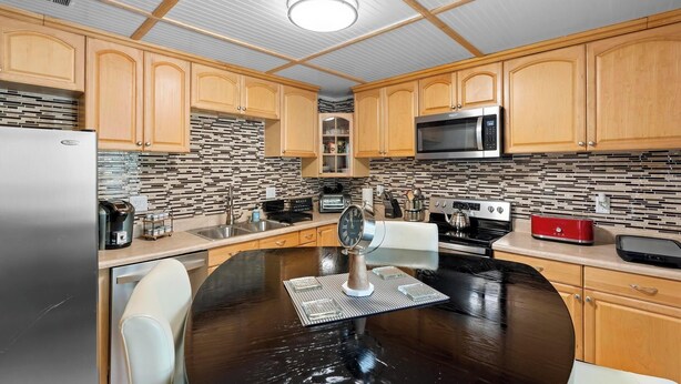 A modern kitchen with wooden cabinets, a black countertop, a stainless steel refrigerator, a microwave, and a coffee maker. - Stylish & Cozy King Bed Retreat @ Baldwin Park (Orlando)
