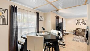 A dining area with a round table, chairs, and a clock. There is a sofa and a TV in the background. - Stylish & Cozy King Bed Retreat @ Baldwin Park (Orlando)