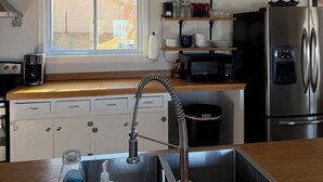 Moderni keittiö, jossa on ruostumattomasta teräksestä valmistettu pesuallas, sisäänrakennettu mikroaaltouuni, jääkaappi ja ikkuna, jossa on sälekaihtimet.