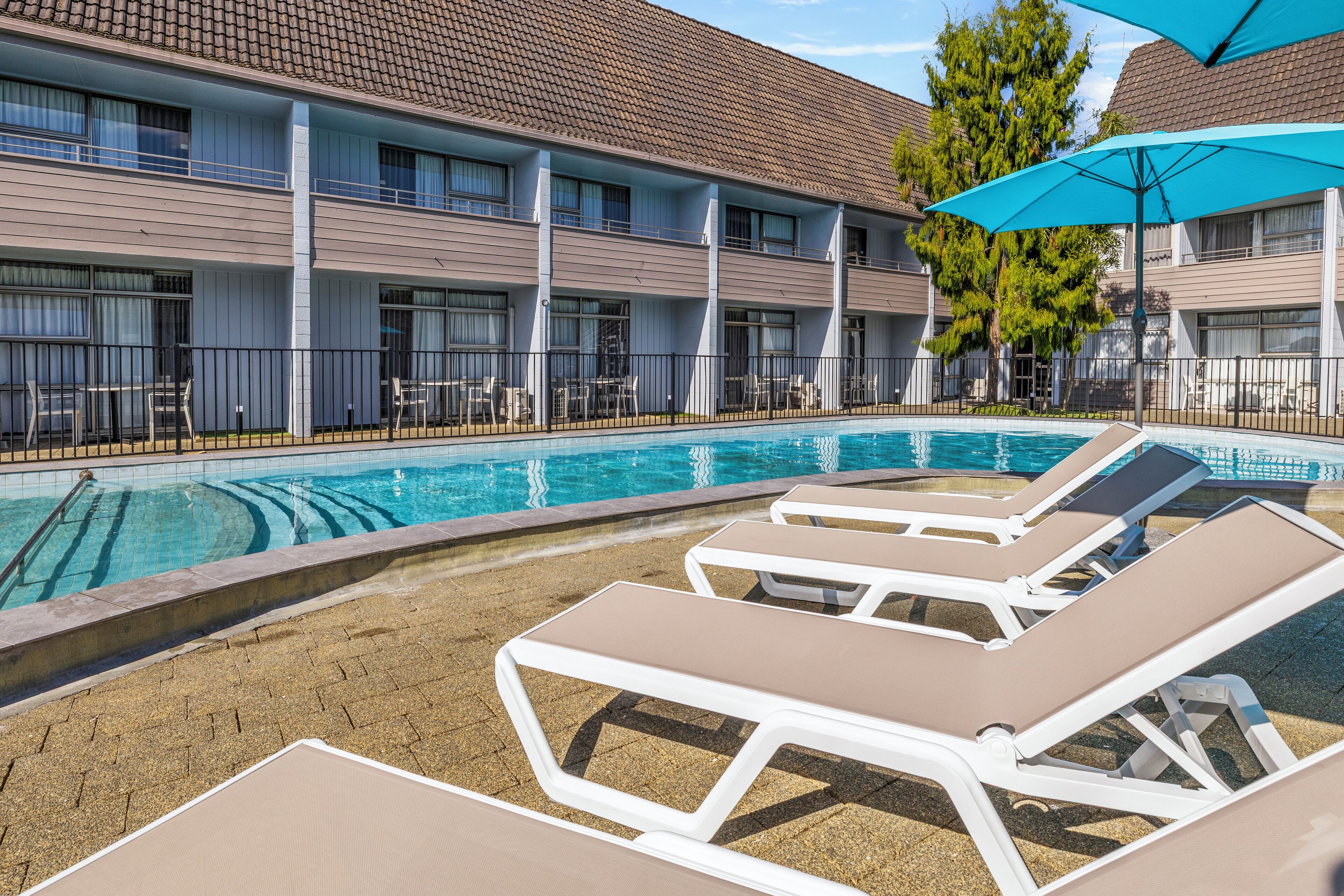A hotel with a swimming pool, lounge chairs, and a covered patio area.