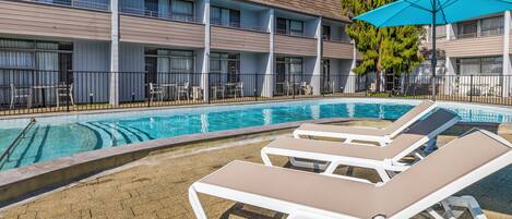 A hotel with a swimming pool, lounge chairs, and a covered patio area.