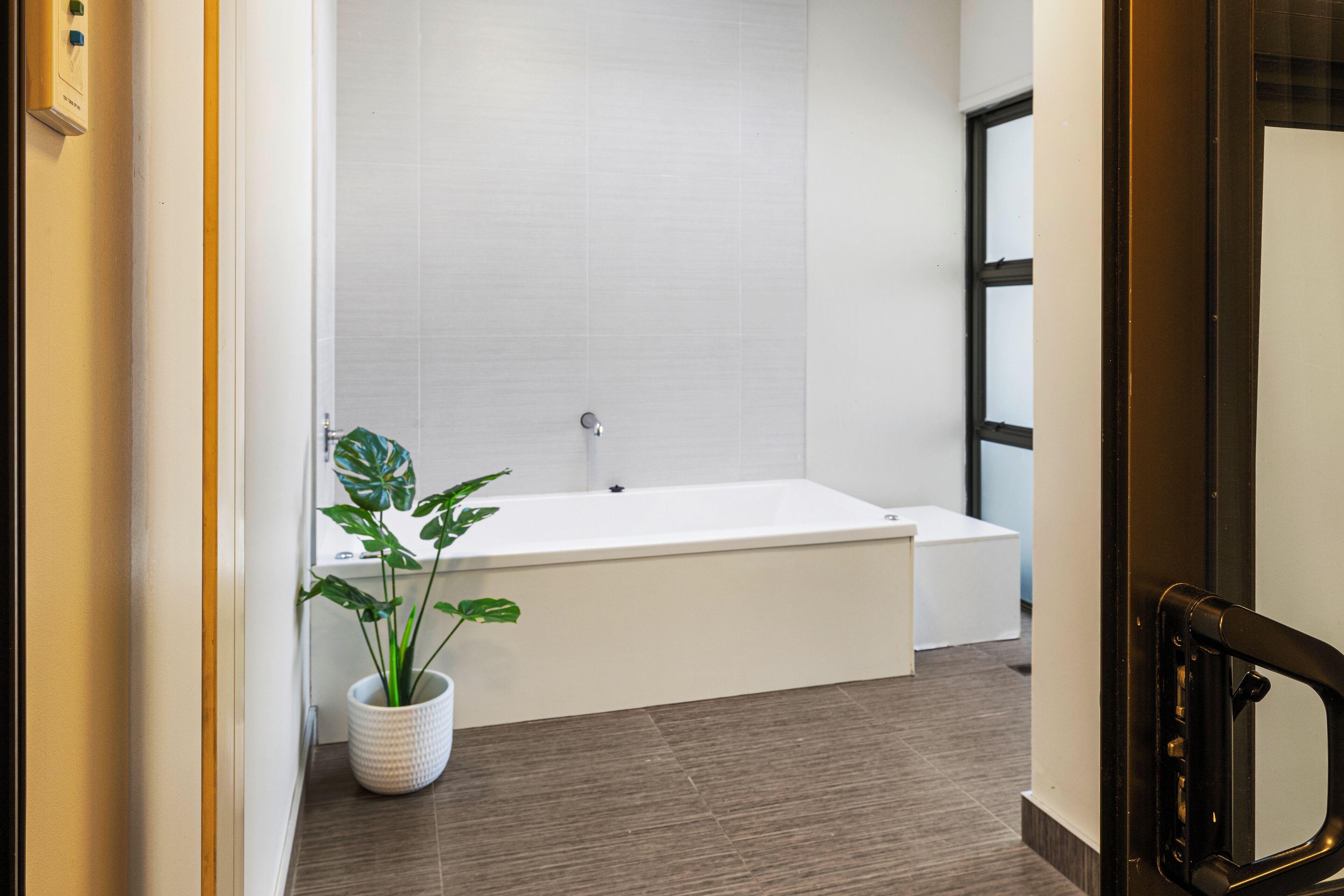 A modern bathroom with a white bathtub, a potted plant, and a large window.