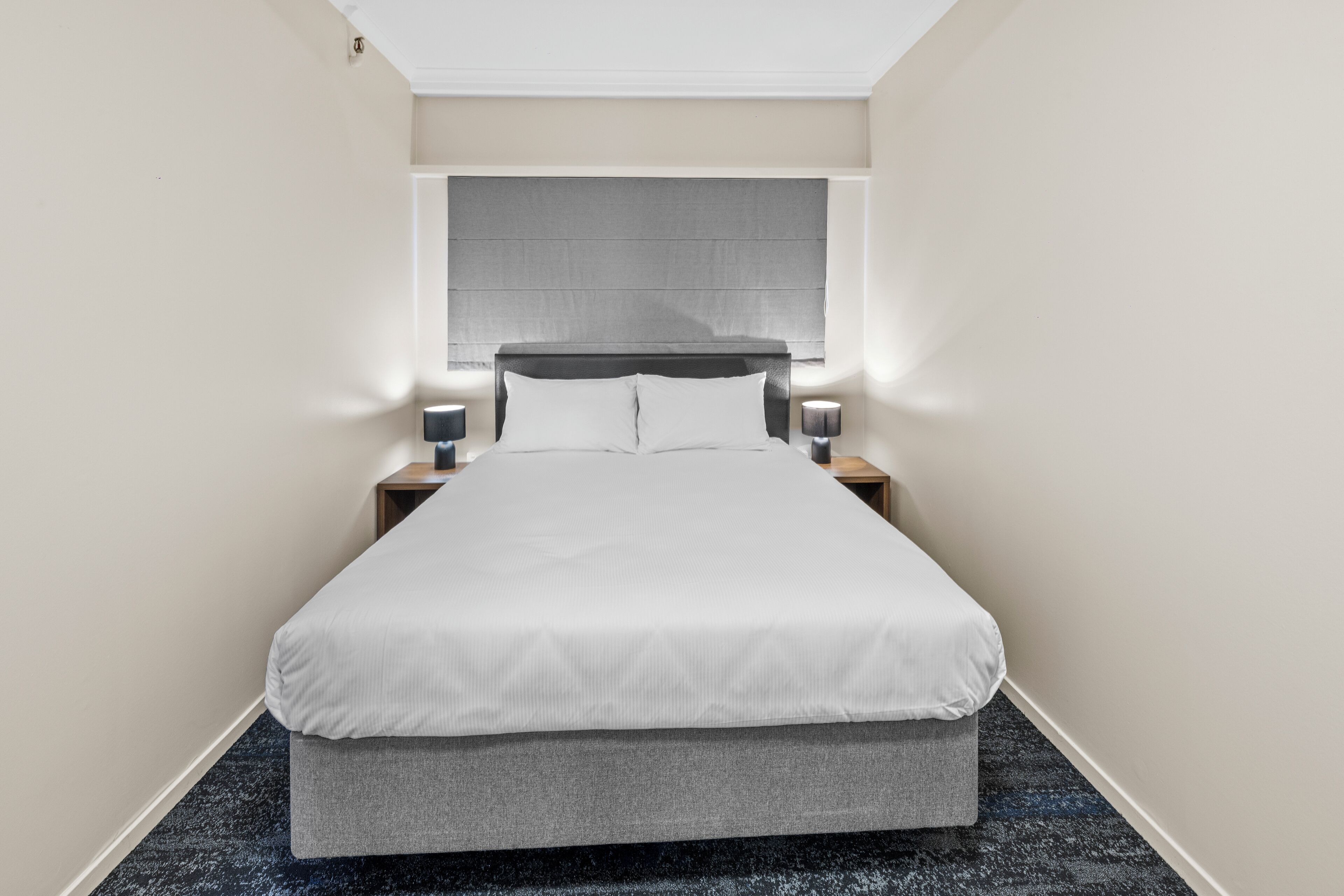 A hotel room with a large bed, a headboard, bedside lamps, and a carpeted floor.