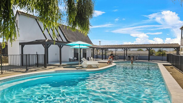 Una piscina con sillas de descanso y sombrillas, rodeada por un área de terraza cubierta.