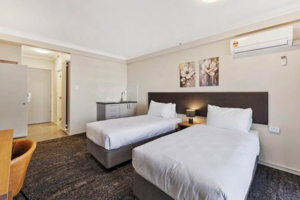 A hotel room with two beds, a desk, a chair, and an air conditioning unit.