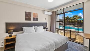 A hotel room with a large bed, a nightstand, a desk, and a view of a swimming pool.